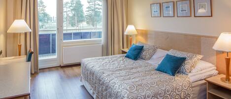Habitación de hotel con una cama grande, dos lámparas de noche, una ventana con cortinas y vista a árboles.