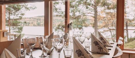 Mesa servida con copas de vino y cubiertos, con vistas a un lago pintoresco.