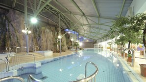 An indoor swimming pool with a tiled floor, metal railings, and a rock wall backdrop.