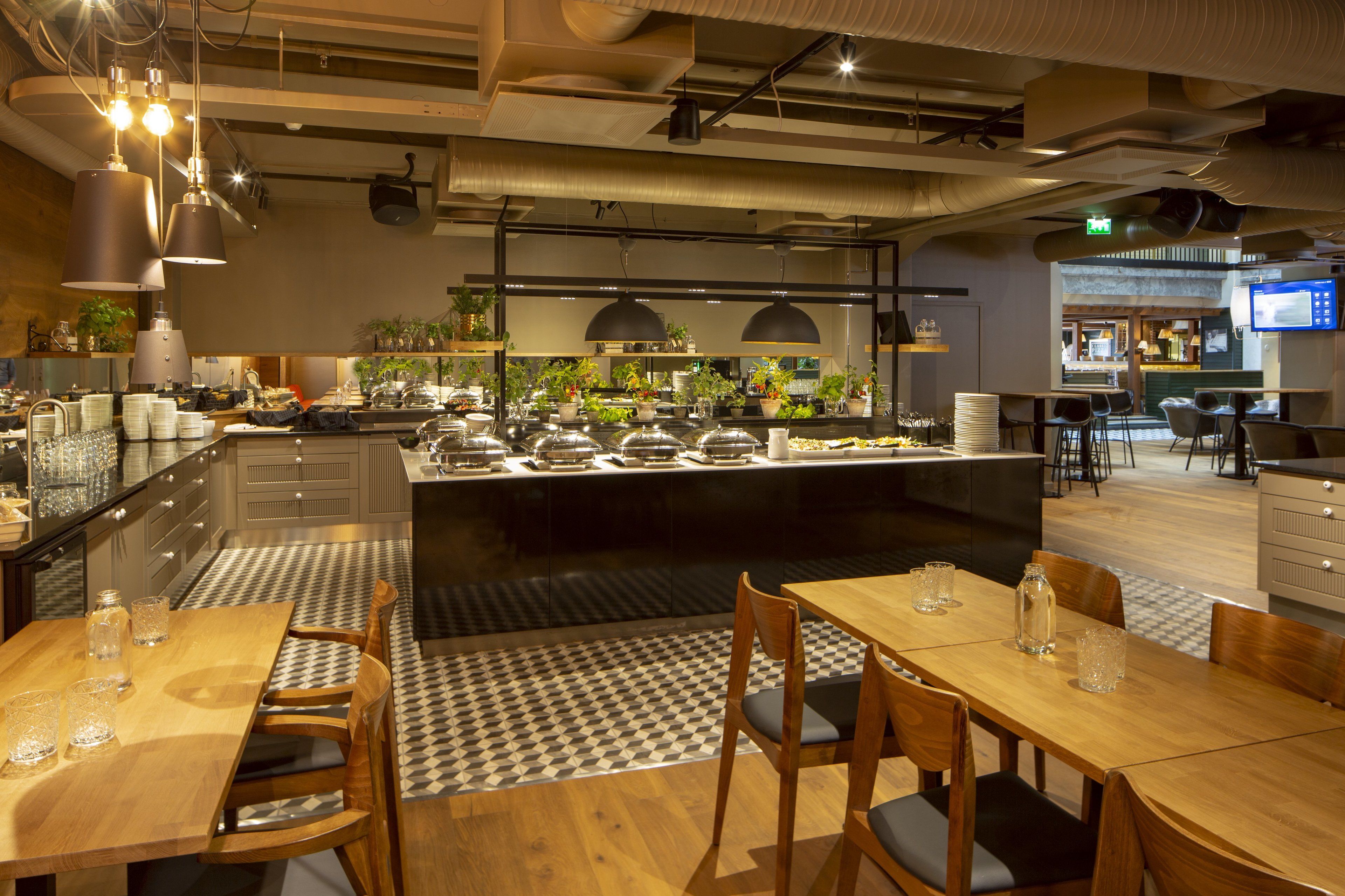 Un restaurante moderno con una isla central, mesas de madera y un suelo con estampado de cuadros.