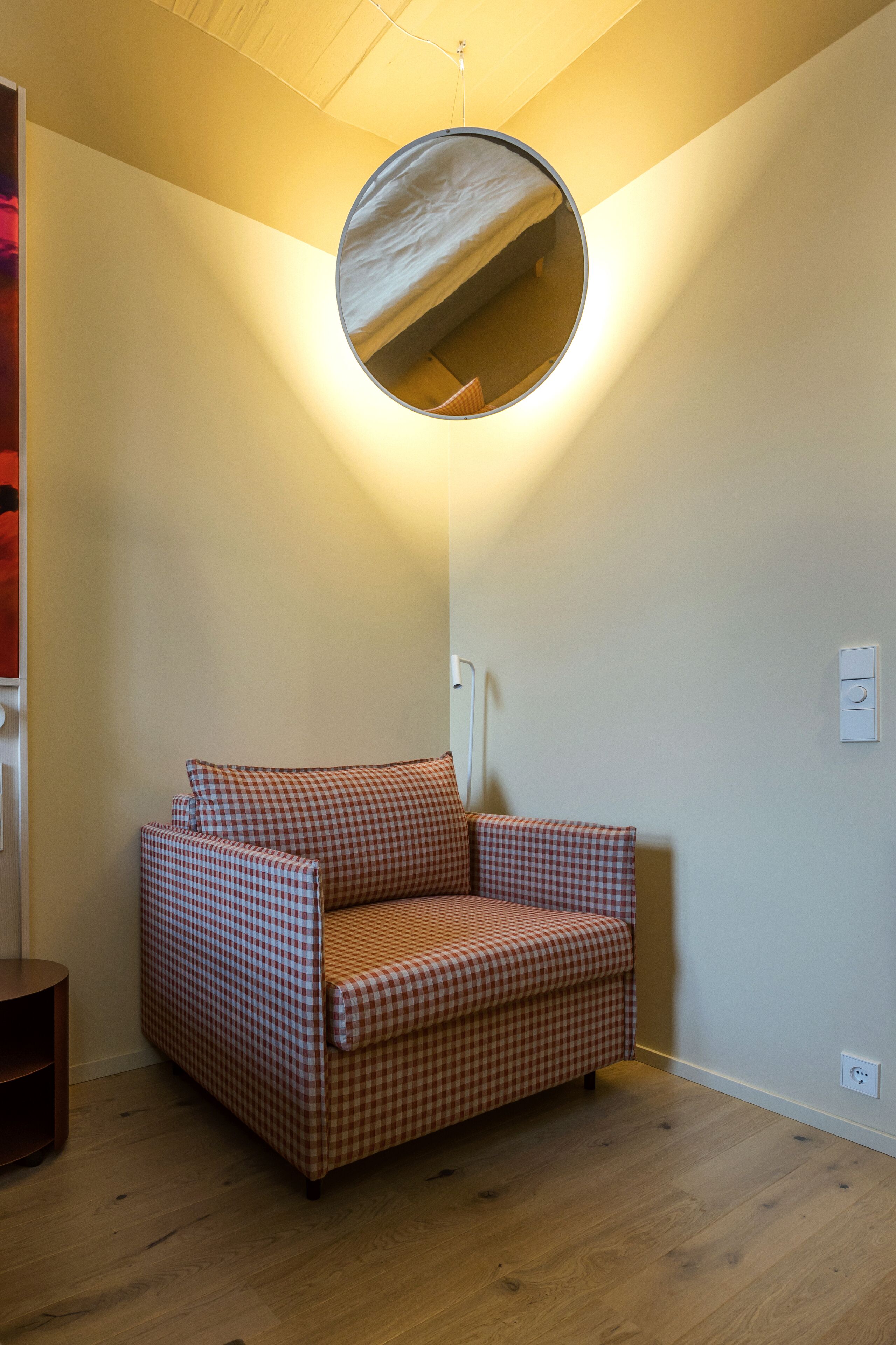 A checkered armchair in a corner with a round mirror on the wall.