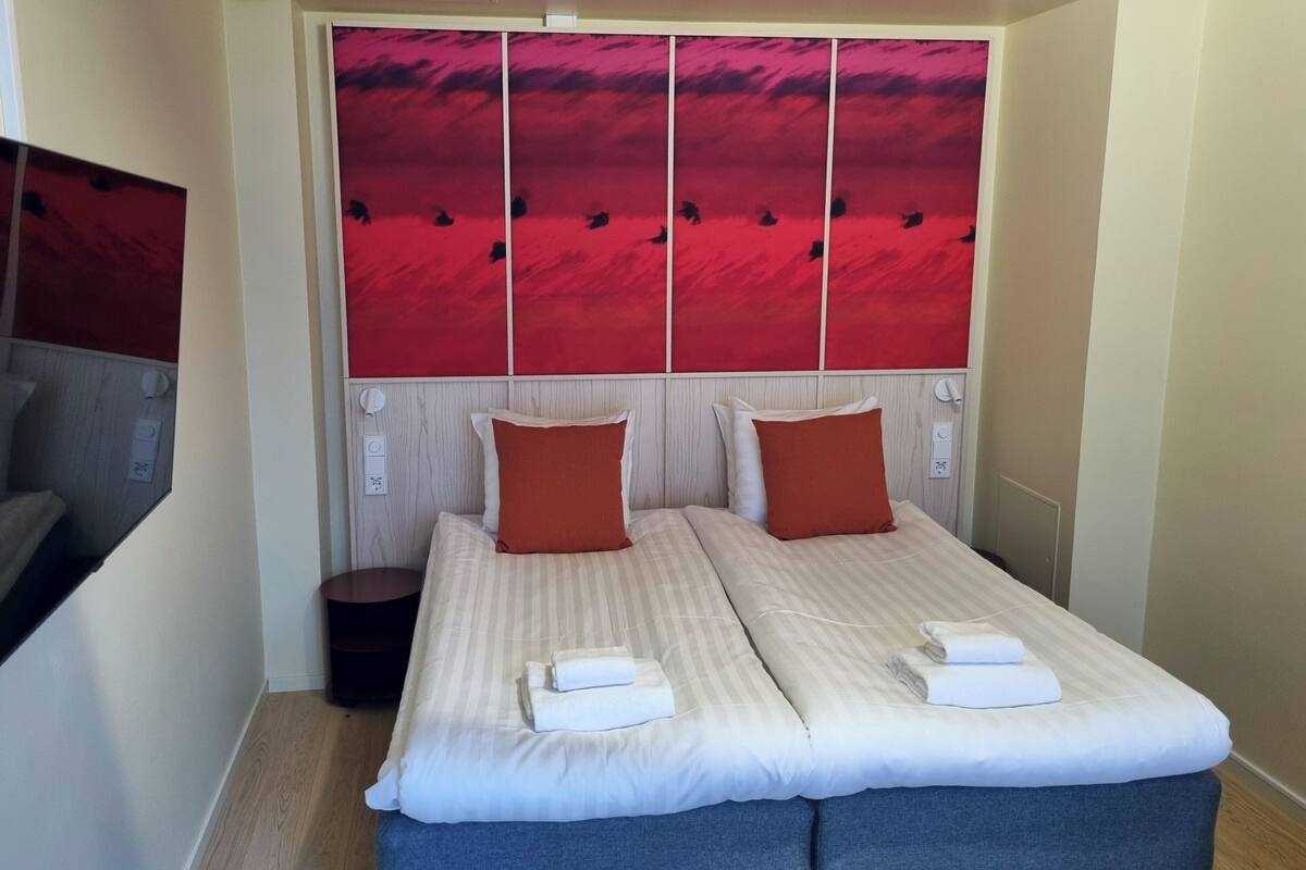 A double bed with two pillows, a bedside table, and a red abstract wall panel.