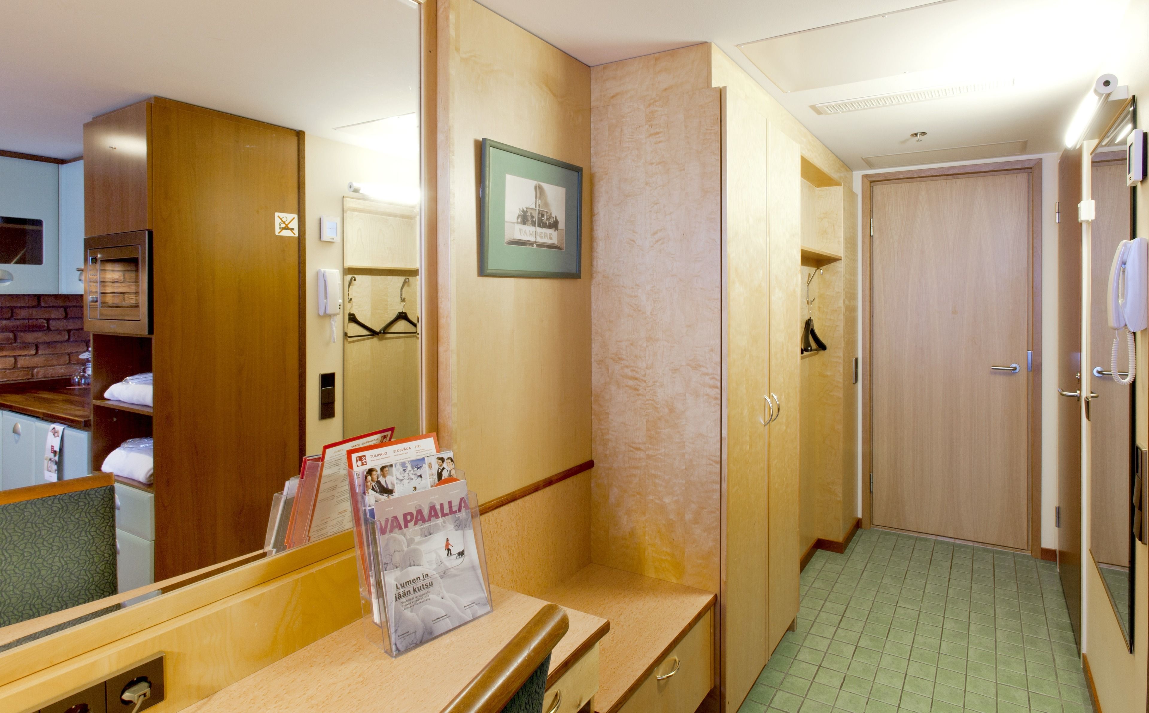 A hotel room with a wooden wardrobe, a mirror, a framed picture, and a magazine rack.