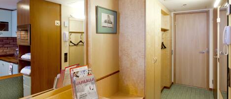 A hotel room with a wooden wardrobe, a mirror, a framed picture, and a magazine rack.