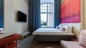 A hotel room with a bed, a desk, a chair, a sofa, a TV, and a window with curtains.