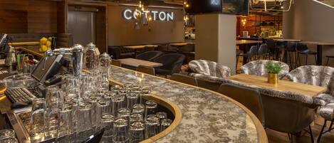A bar area with a counter, stools, and a seating area with a 'COTTON' sign.