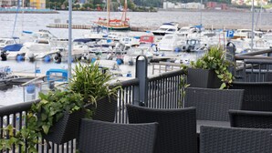 A marina with boats, a tower in the background, and outdoor seating with plants.