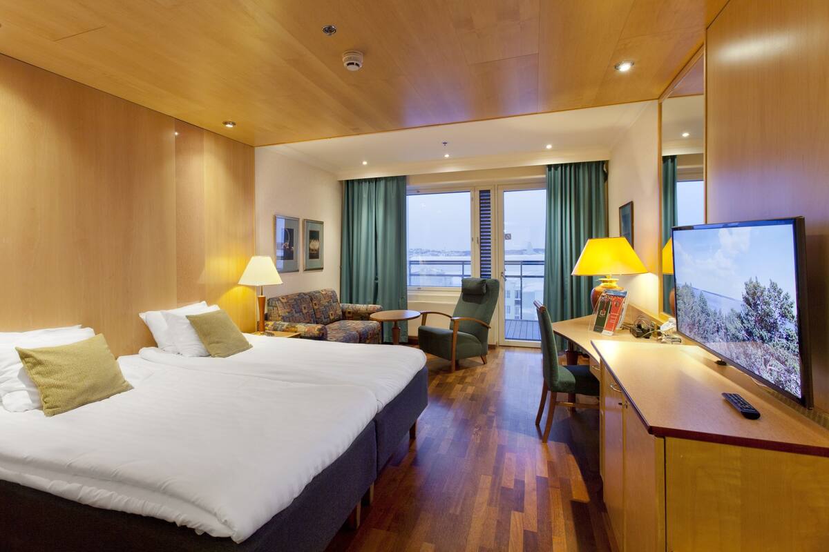 A hotel room with a large bed, a desk with a computer, a chair, and a view of the city through the window.