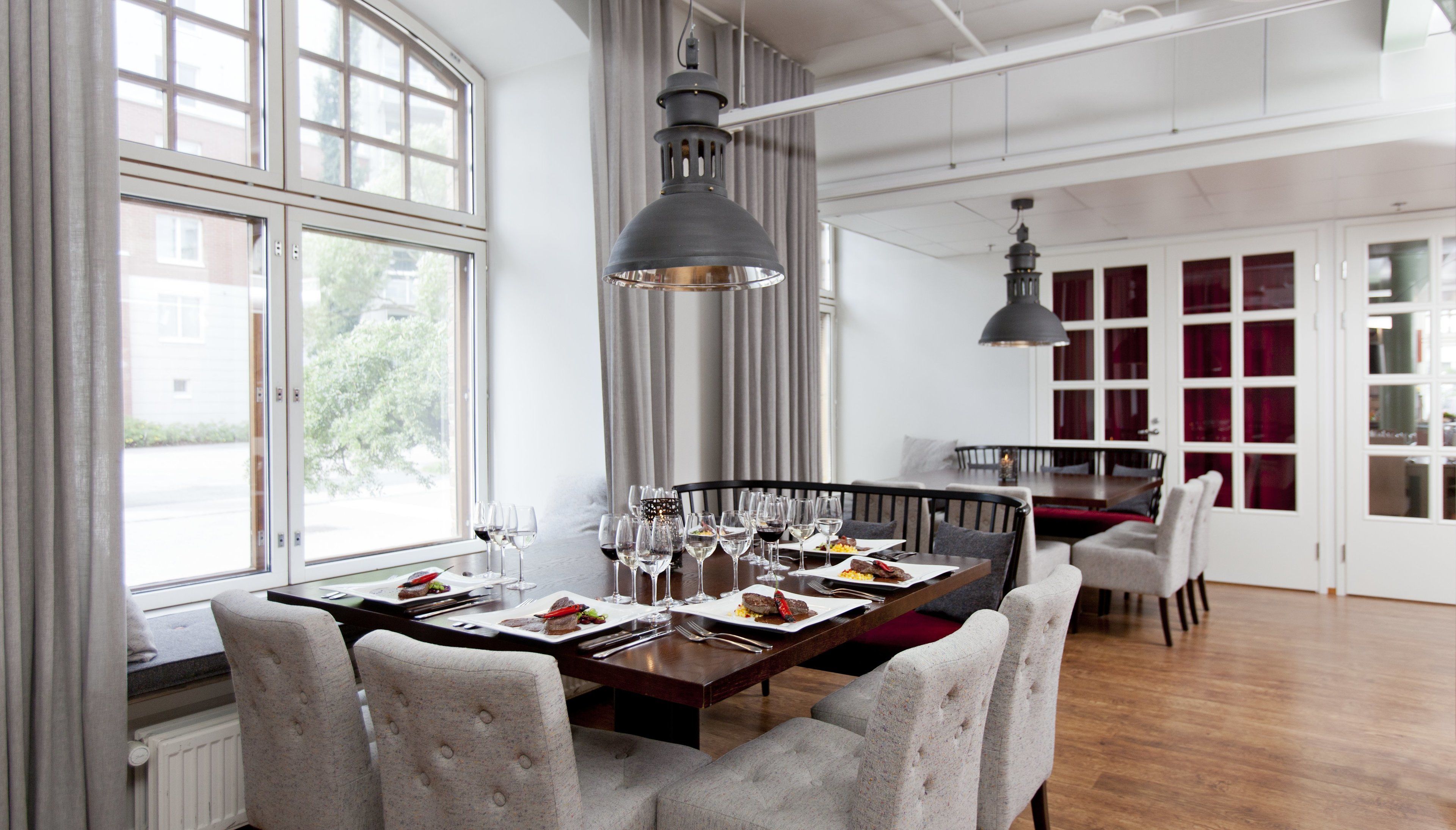 A dining area with a long table set for a meal, large windows, and a view of the outside.