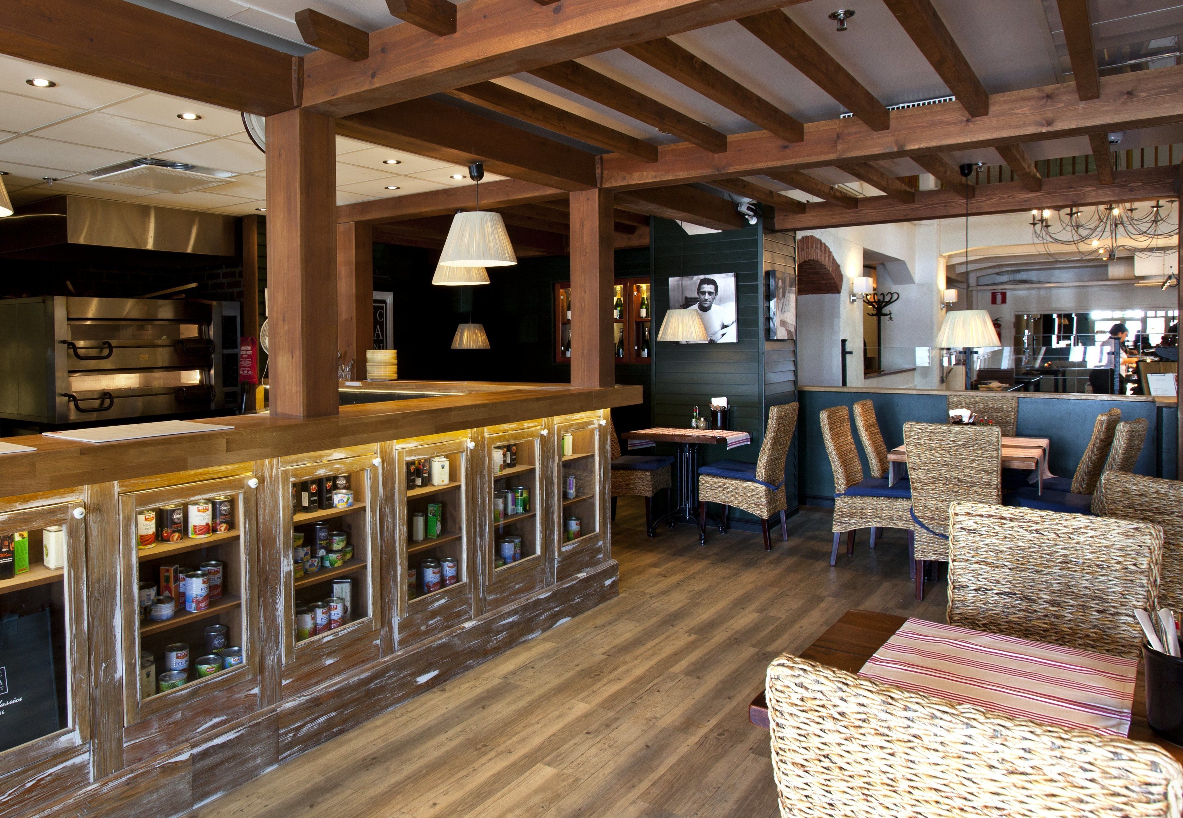 Un comptoir en bois avec des étagères remplies de bouteilles et un espace salon avec des fauteuils en osier.