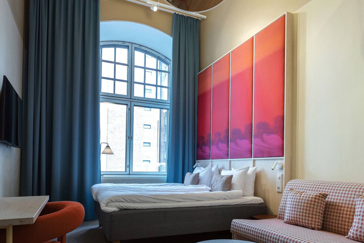 A modern hotel room with a bed, a sofa, a round table, and a desk.