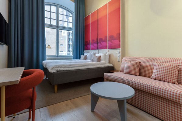 A modern hotel room with a bed, a sofa, a round table, and a window with curtains.