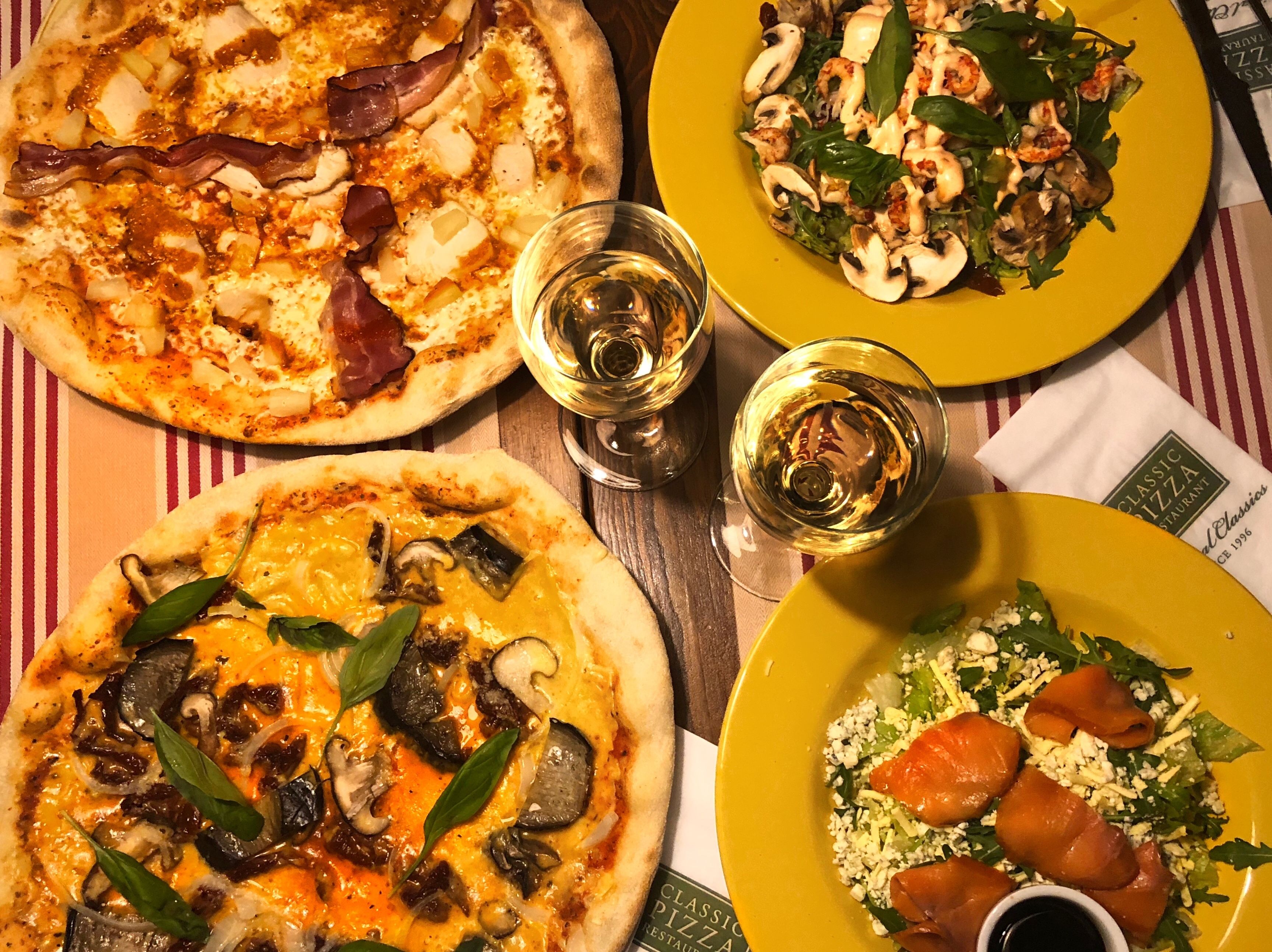 Trois pizzas et une salade sur une table recouverte d’une nappe à rayures.