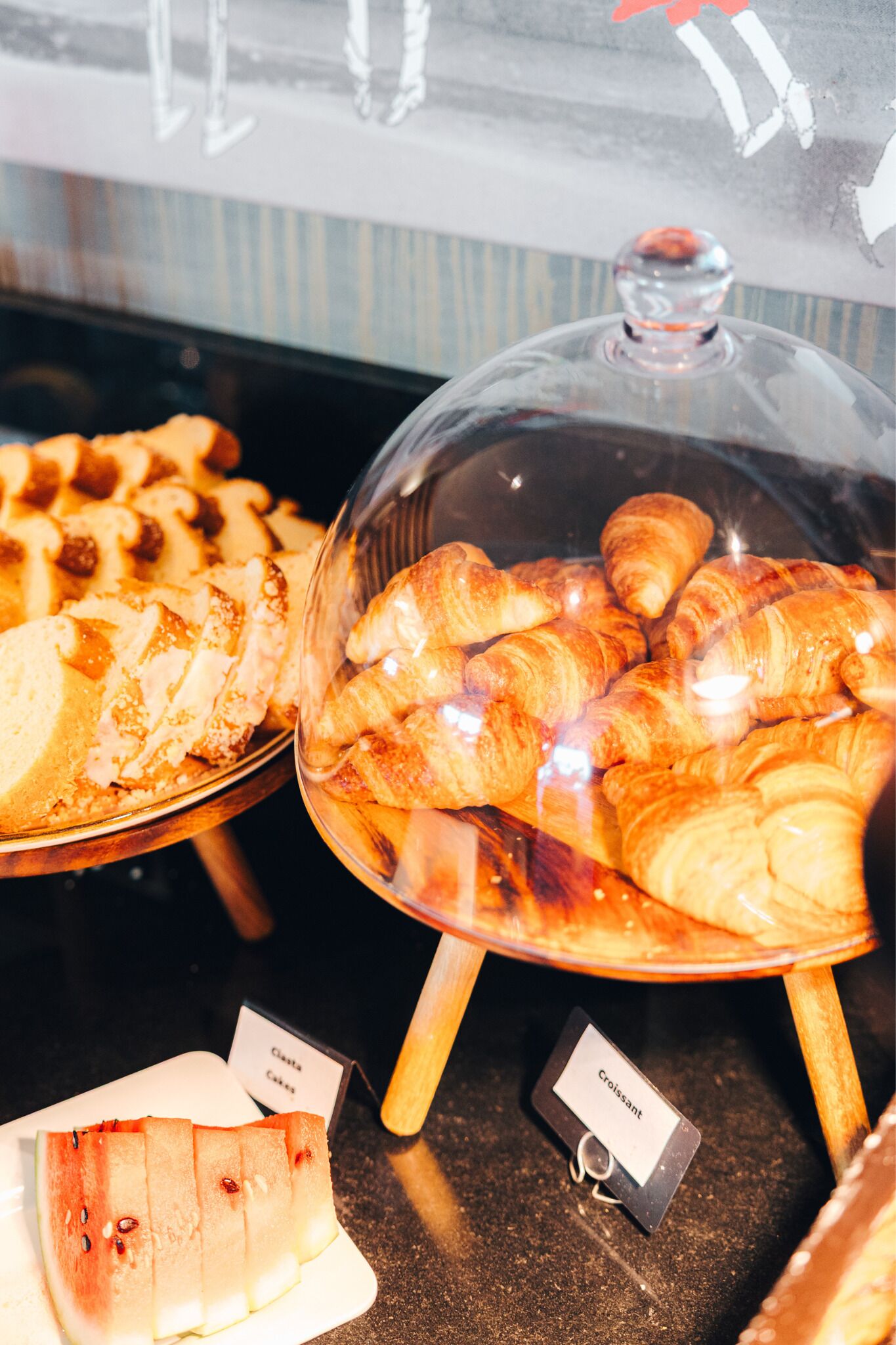 Una vitrina con varias opciones de repostería, incluyendo cruasanes y una tarta en porciones.