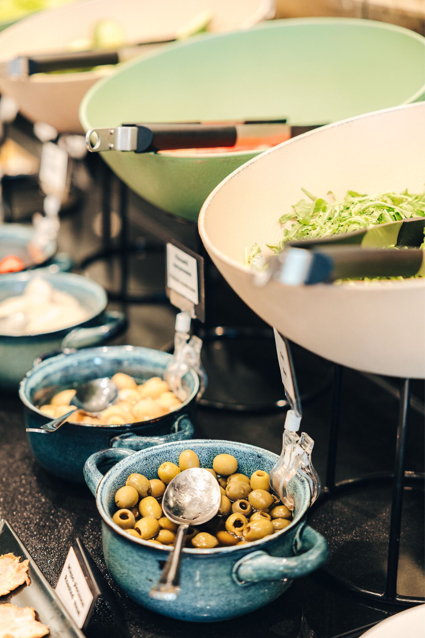 Een buffet met diverse gerechten, waaronder schalen met olijven en een grote saladekom.