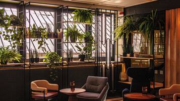 A modern interior with a seating area, large windows with plants, and a dark-toned wall.