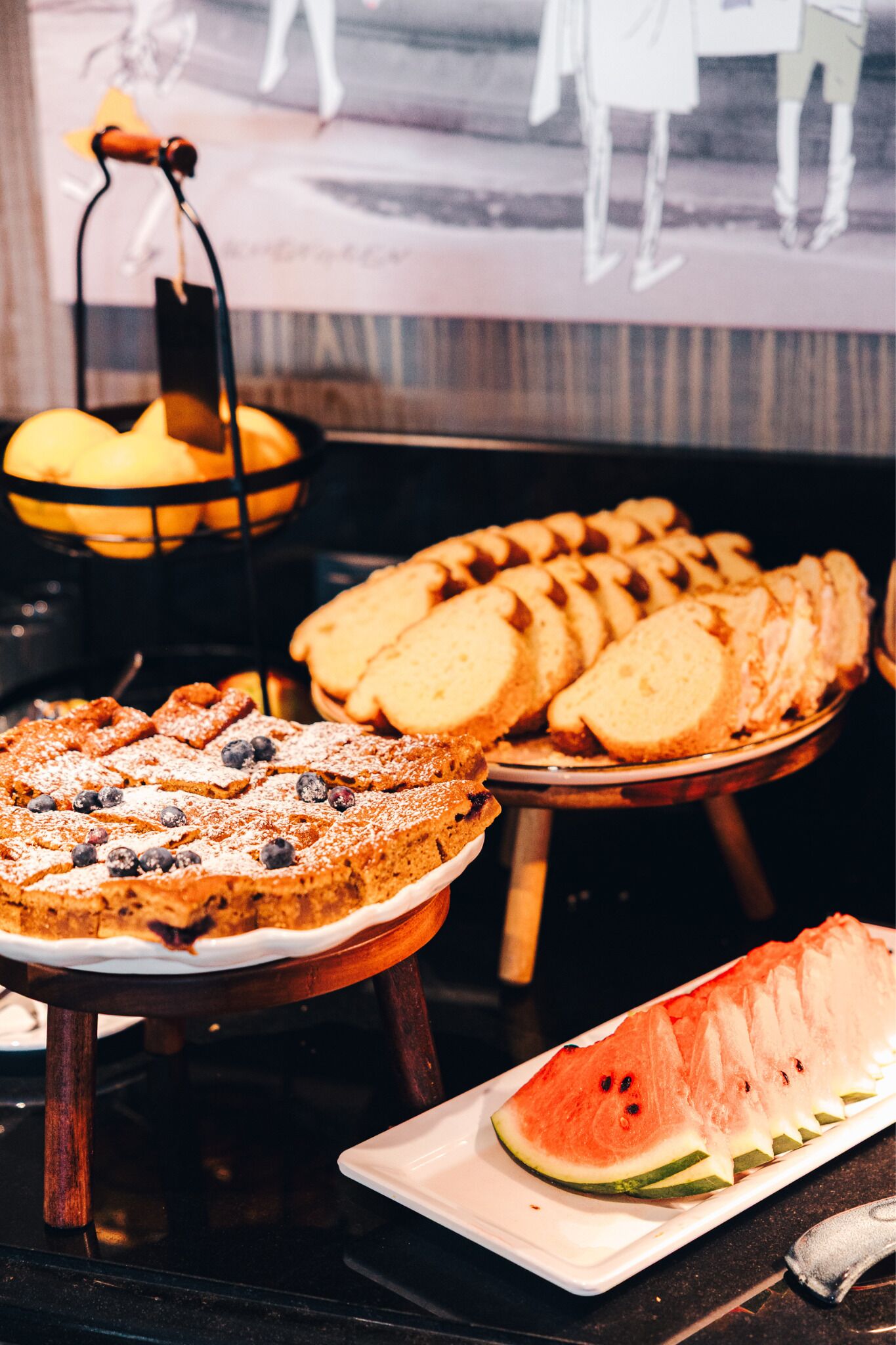 Ein Buffet mit verschiedenen Desserts, darunter ein Kuchen mit Blaubeeren, Brotscheiben und Wassermelonenscheiben.
