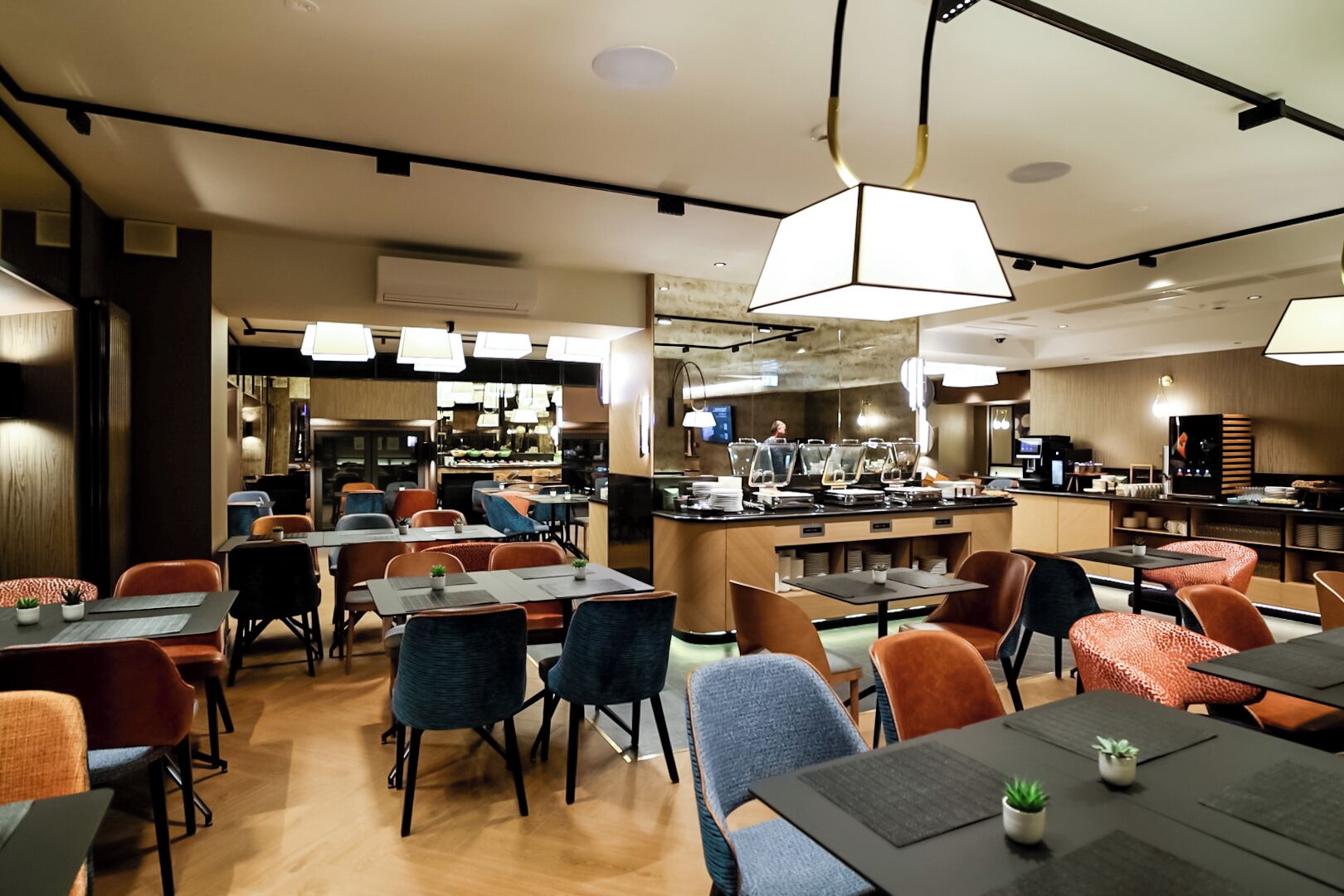 Un restaurant moderne doté d’un bar central, de plusieurs types de sièges, notamment des tables et des banquettes, et d’une cuisine ouverte visible à l’arrière.
