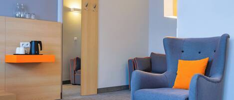 A modern room with a wooden cabinet, a blue armchair with an orange cushion, and a coffee maker on a shelf.