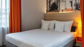Una cama bien tendida con sábanas y almohadas blancas, un cabecero de madera y una lámpara fijada a la pared.
