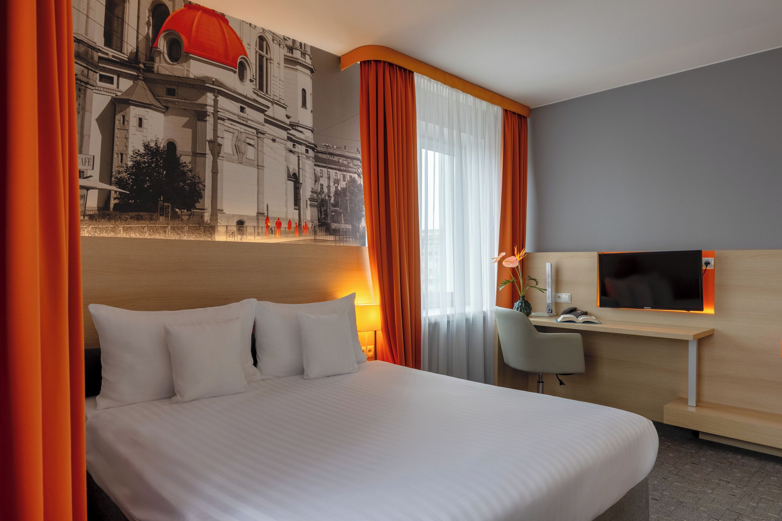 A hotel room with a large bed, a desk with a TV, and a mural on the wall.