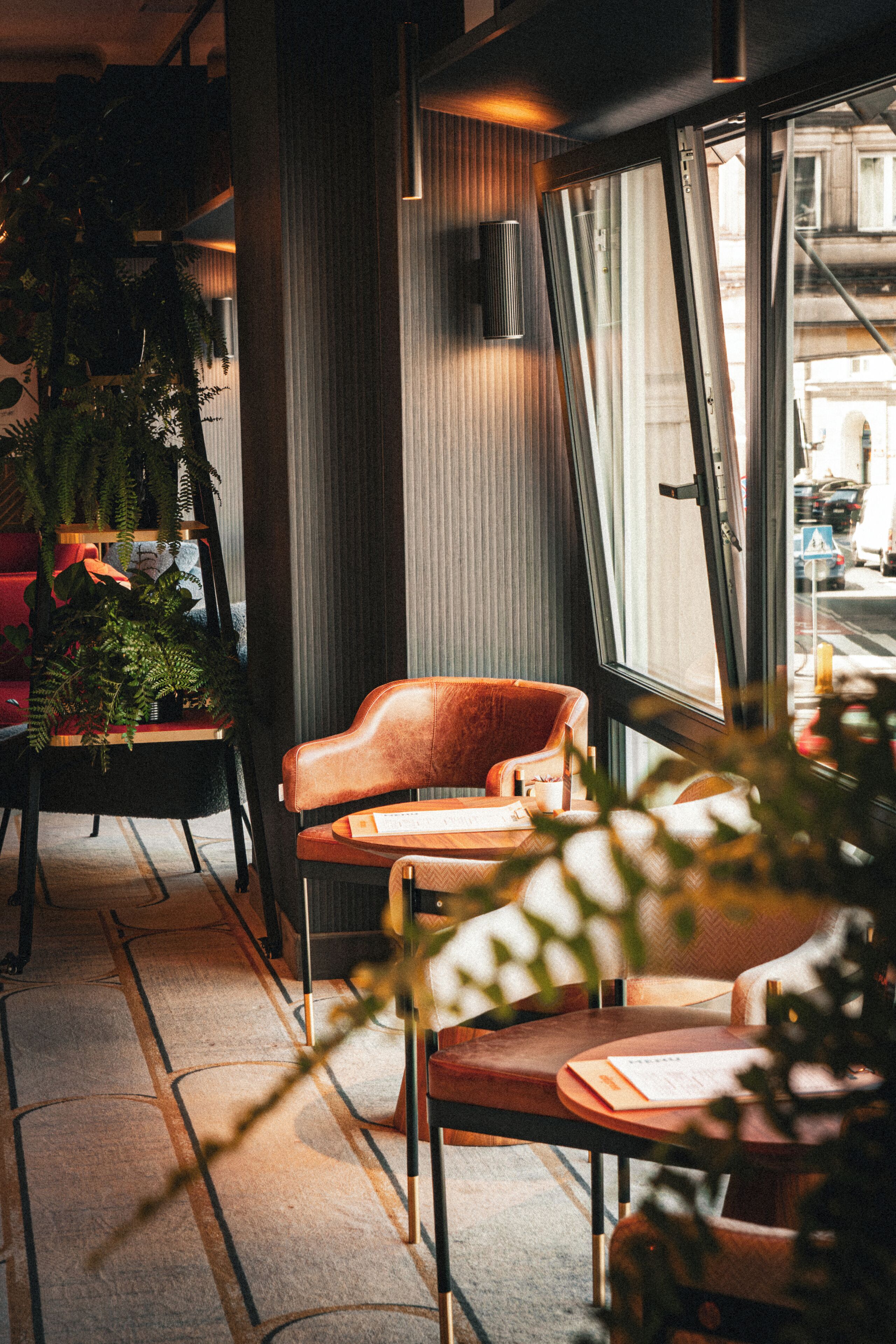 A cozy seating area with a leather chair and a table, a potted plant, and a window with a view of the street.