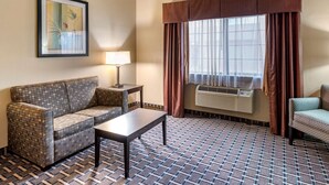 Ein Hotelzimmer mit gemustertem Boden, einer Couch, einem kleinen Tisch, einer Lampe, einem Fenster mit Vorhängen und einer Klimaanlage.