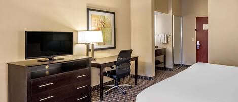 A hotel room with a bed, a desk with a TV, a chair, a lamp, and a painting on the wall.