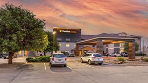 Ein Comfort Suites Hotel mit Parkplatz, einem großen Baum und einem Sonnenuntergangshimmel.