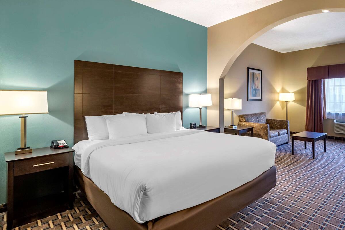 Una habitación de hotel con una cama grande, dos mesitas de noche con lámparas, una silla y una pequeña mesa.