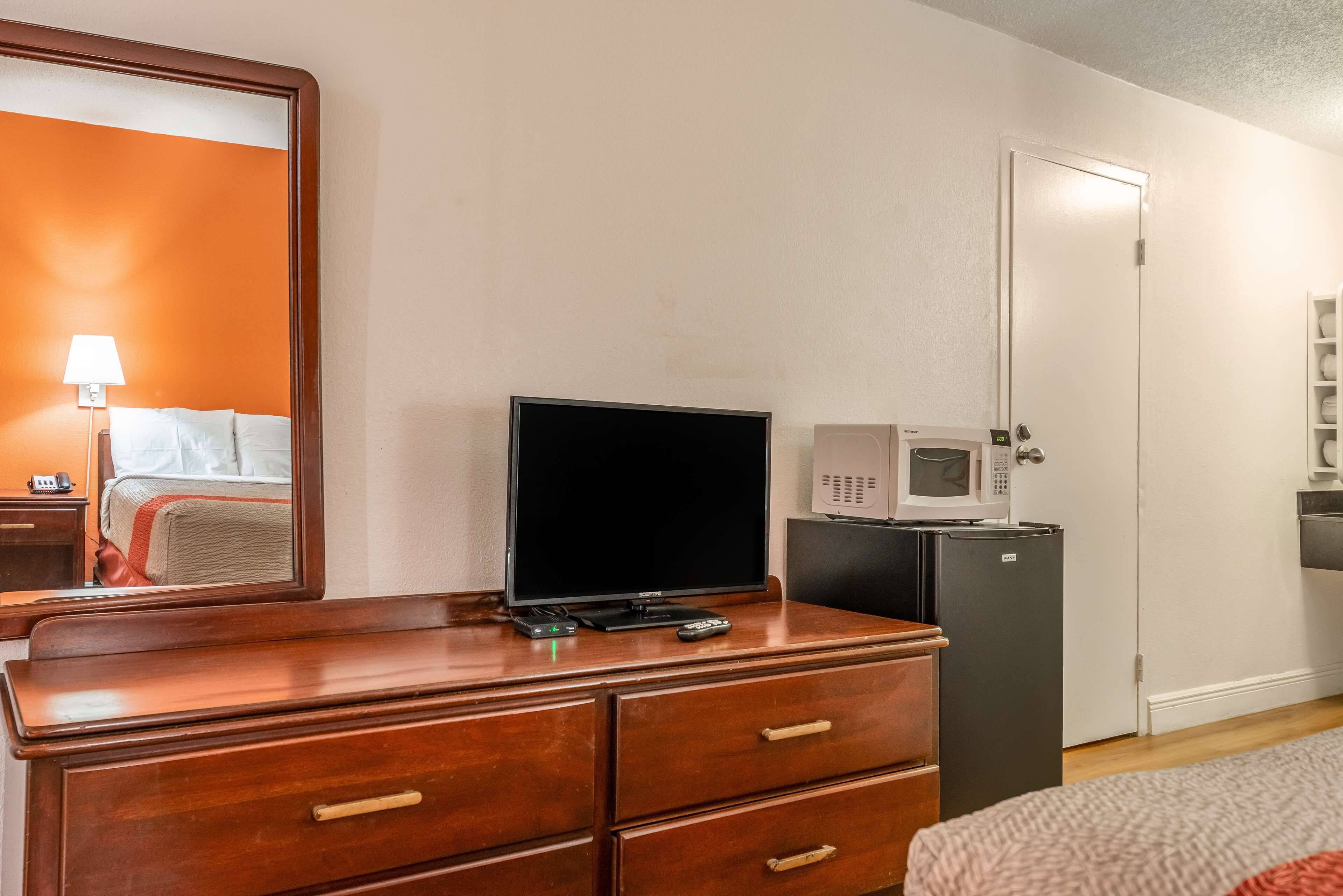 Une chambre d’hôtel avec une commode en bois, un téléviseur, un four à micro-ondes et une porte.