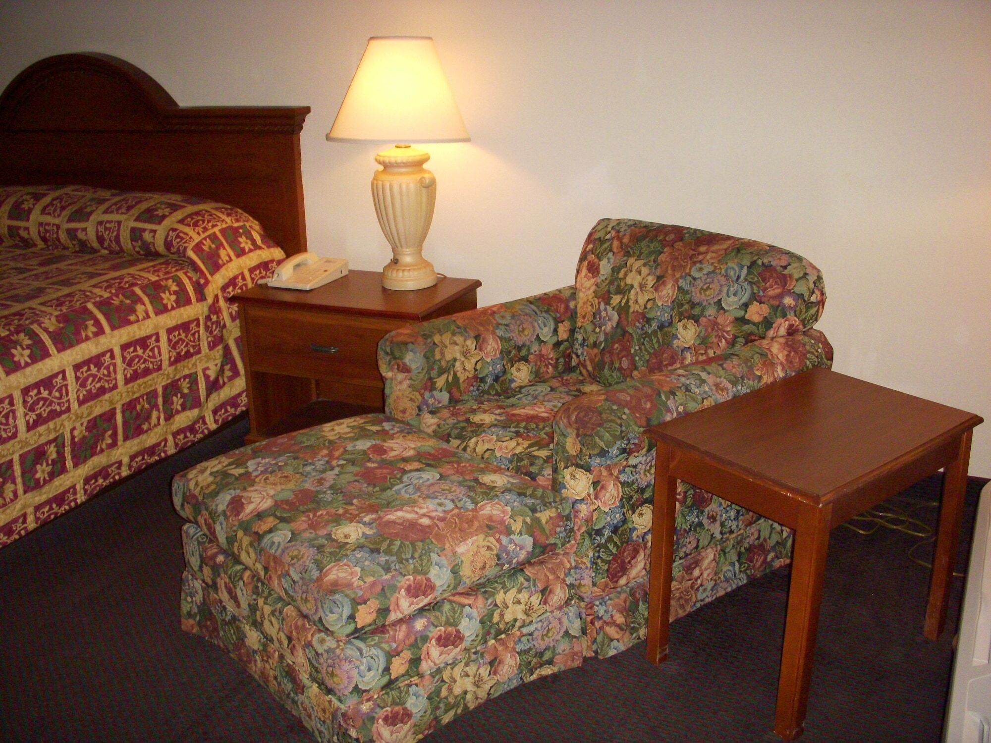 A hotel room with a bed, a chair, a small table, and a lamp.