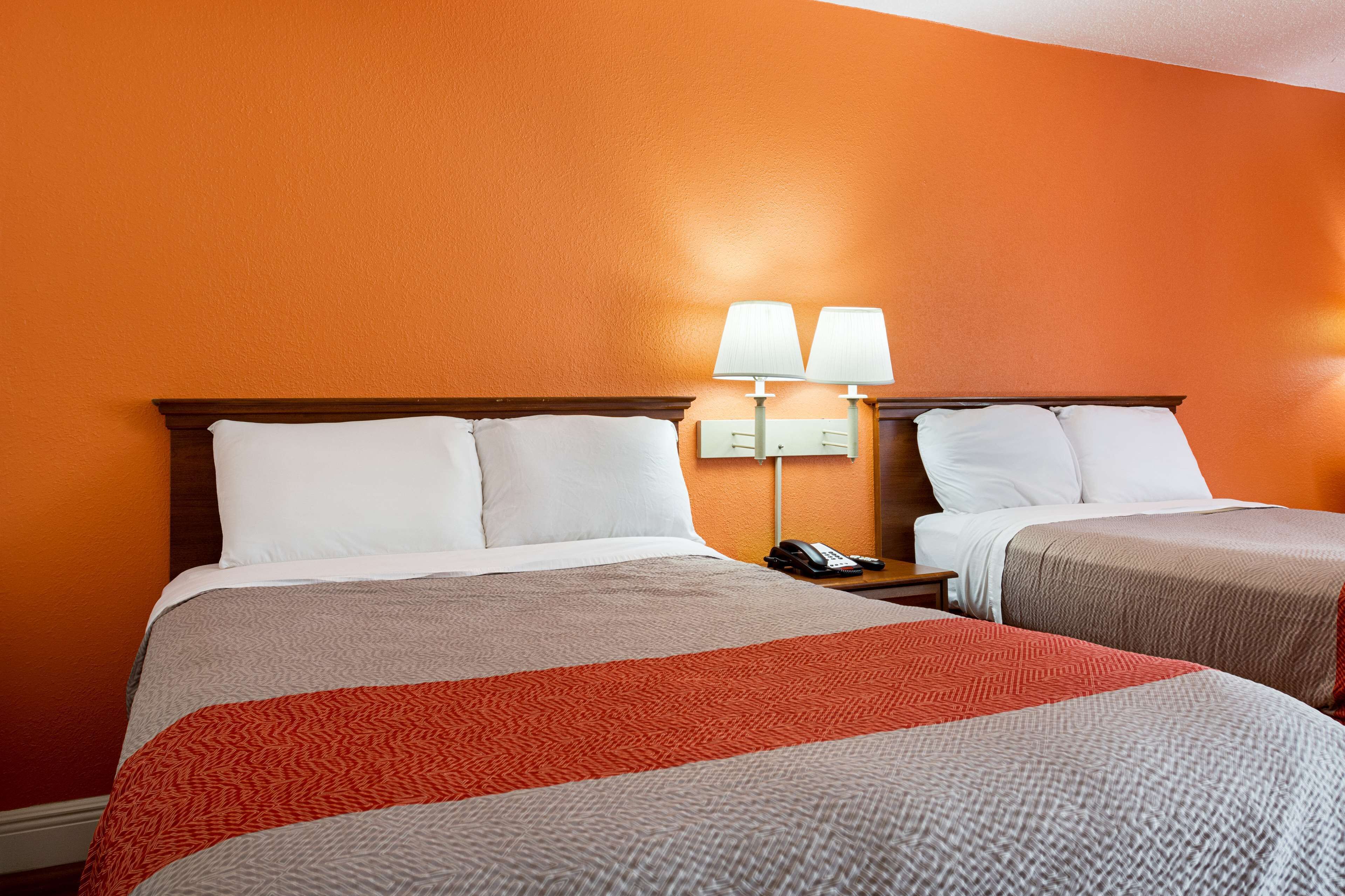 Habitació d'hotel amb dos llits, parets taronges i una taula de nit amb una làmpada i un telèfon.