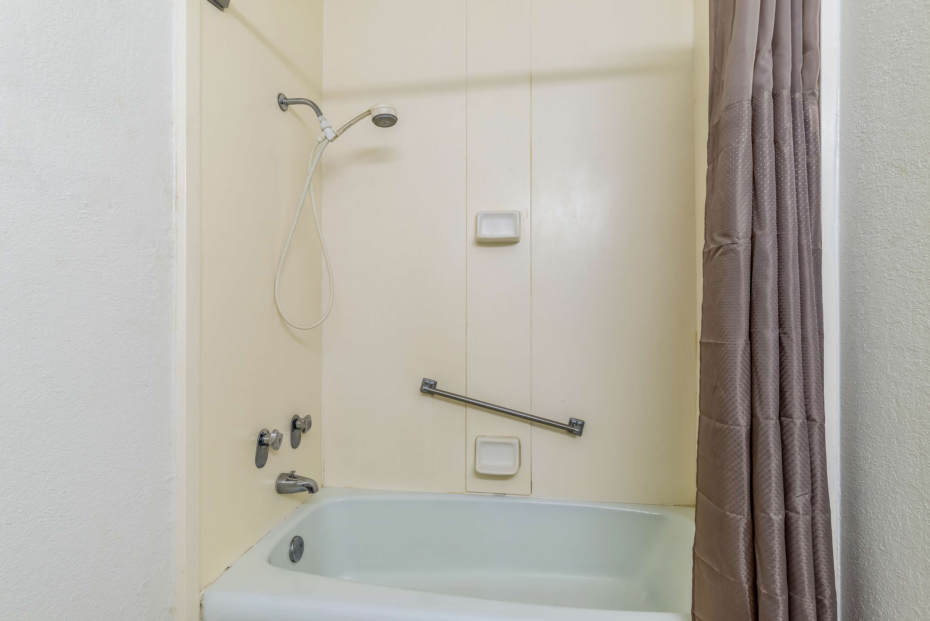A bathroom with a bathtub, a shower, and a handrail.