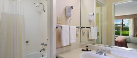A bathroom with a bathtub, a sink, a hairdryer, and a large mirror.