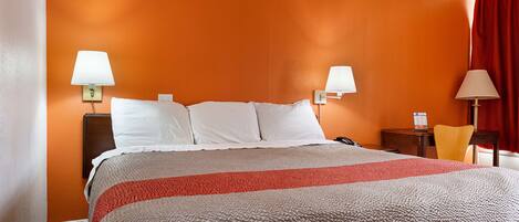 Une chambre d’hôtel avec un mur orange, un lit avec une literie blanche et rouge, deux lampes de chevet, une table de chevet en bois et un rideau rouge.