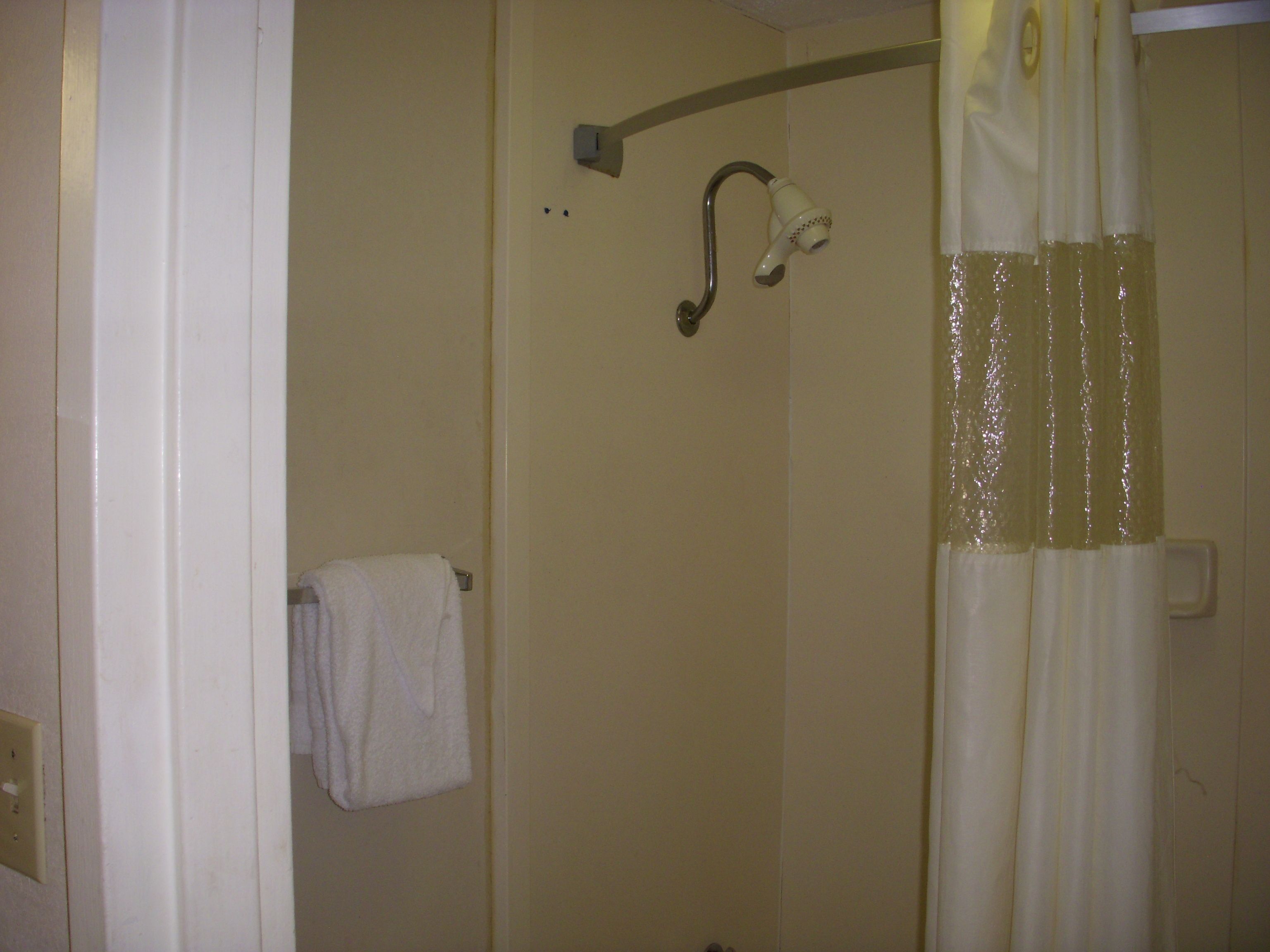 A bathroom with a shower curtain, a towel rack with a towel, and a wall-mounted light fixture.