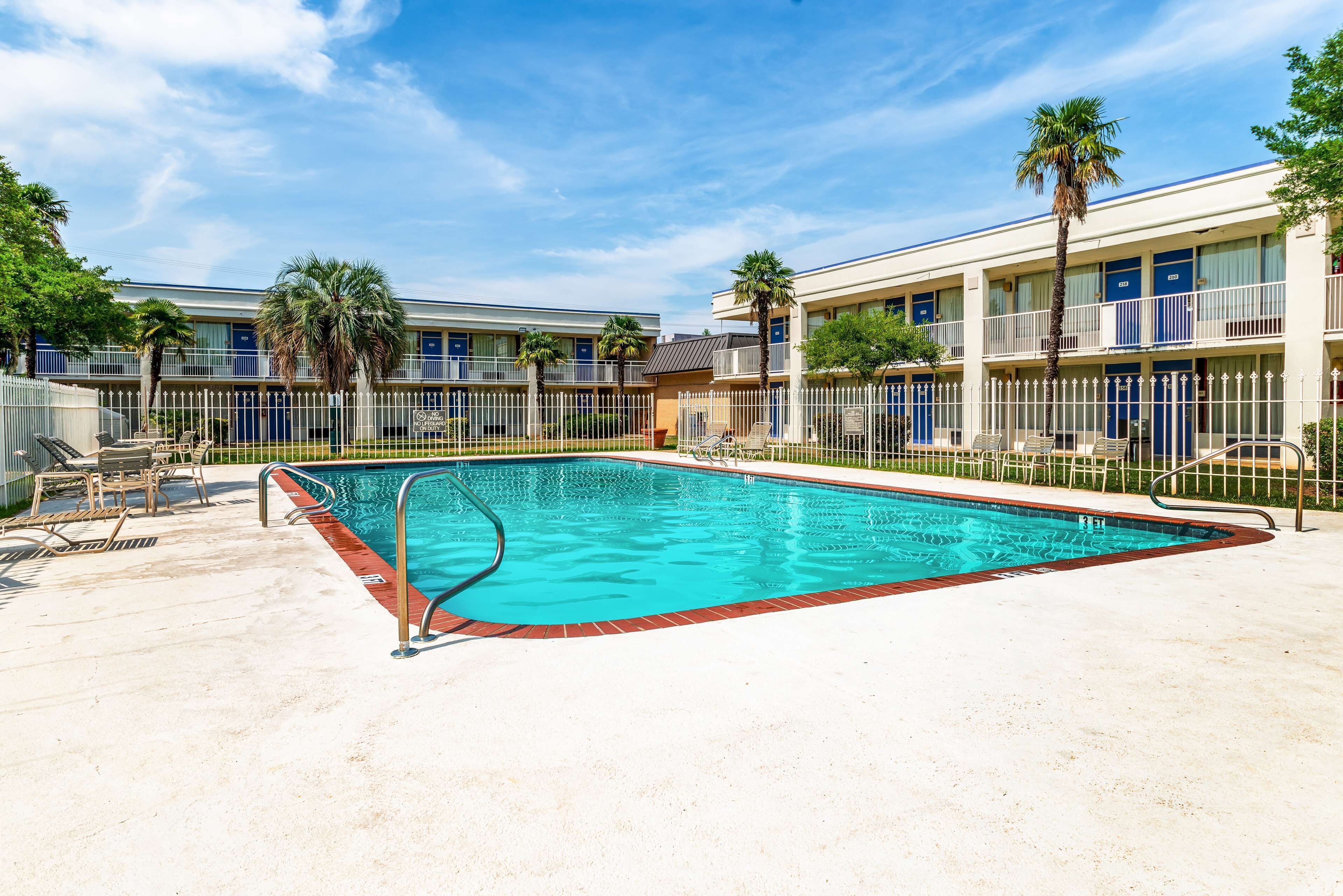 Una piscina con valla blanca, palmeras y un edificio con varios balcones.