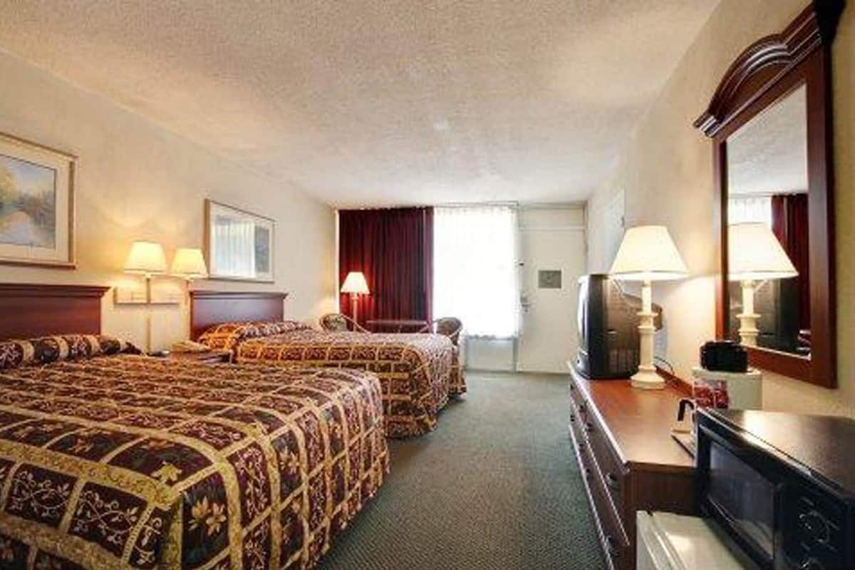 A hotel room with two beds, a television, a desk, and a mirror.