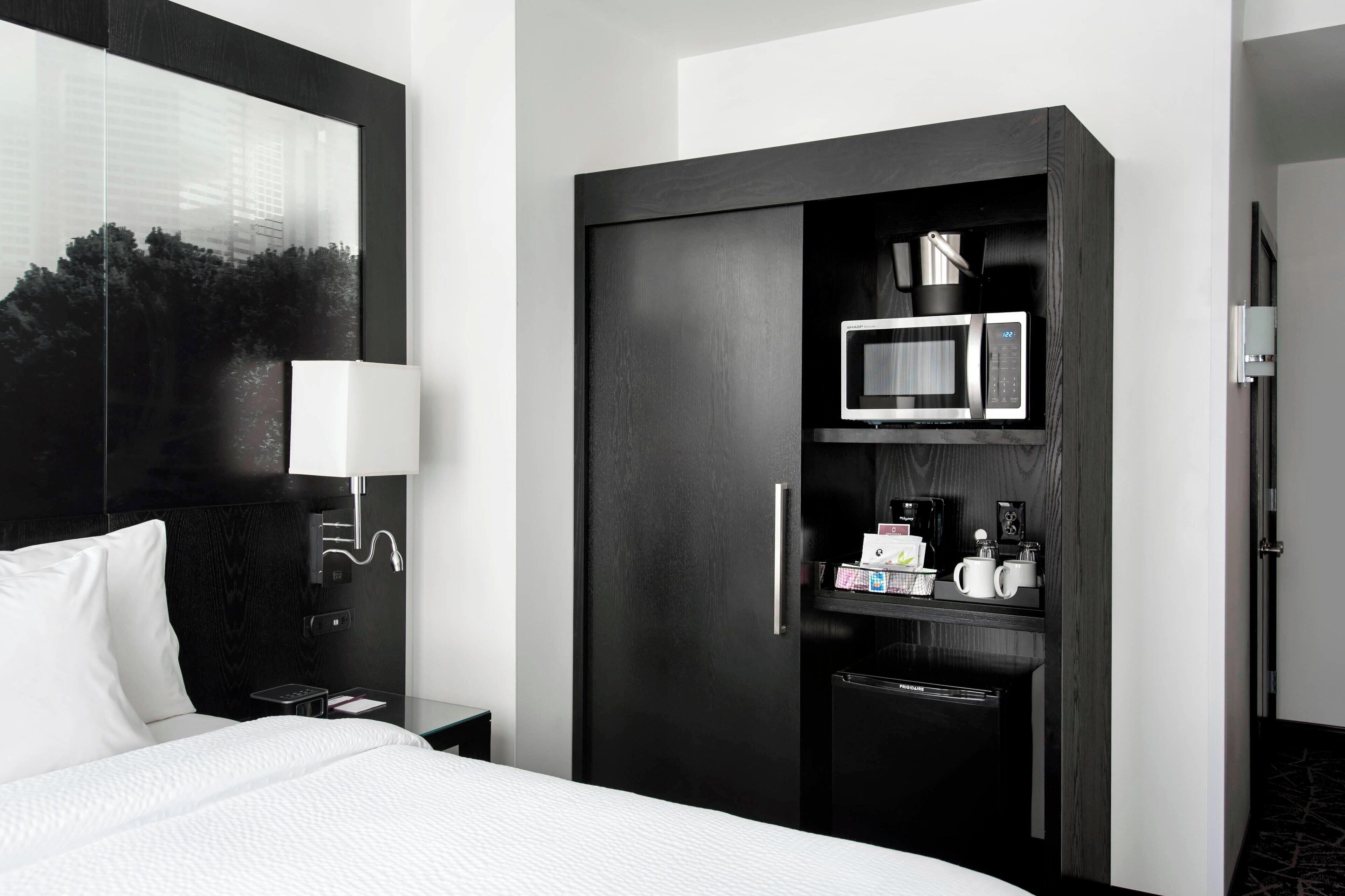 Una habitación de hotel con una cama, un armario de madera oscura que incluye un microondas, una cafetera y un refrigerador pequeño.
