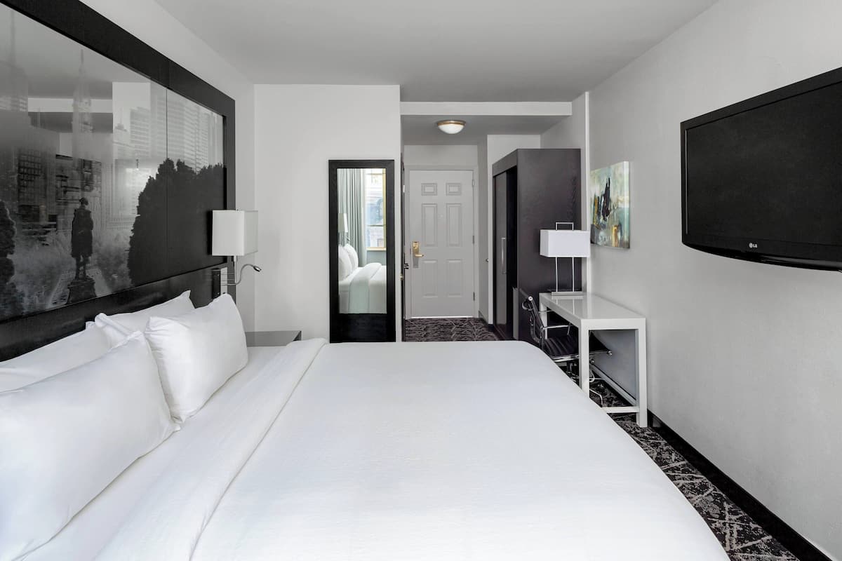 A hotel room with a large bed, a desk, a flat-screen TV, and a door leading to a bathroom.