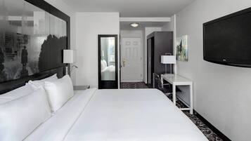 A hotel room with a large bed, a desk, a flat-screen TV, and a door leading to a bathroom.