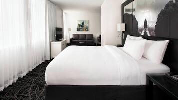 A hotel room with a large bed, a flat-screen TV, a sofa, and artwork on the walls.