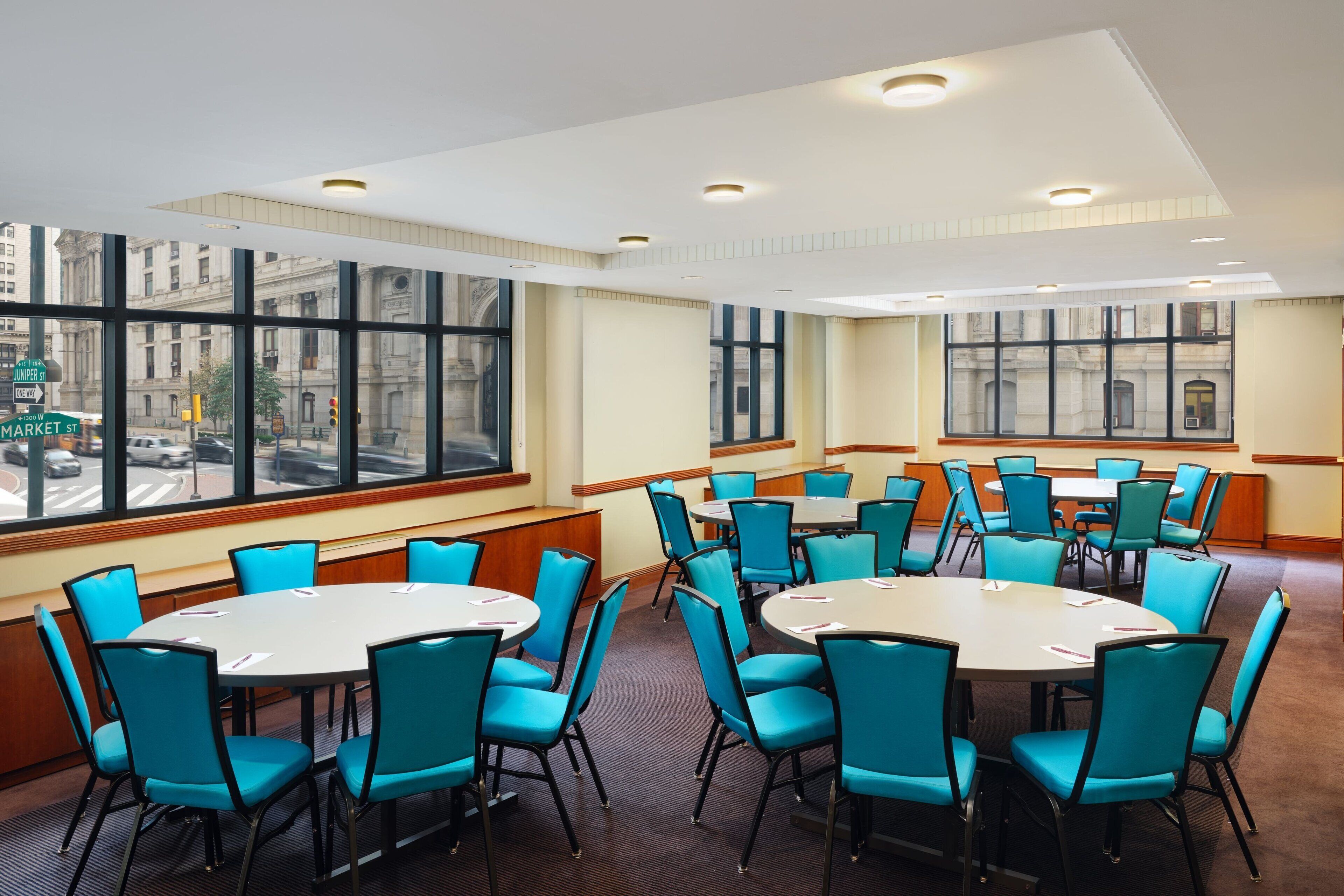 A conference room with round tables and blue chairs, large windows with city views, and a modern ceiling design.