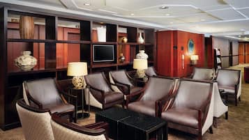 A hotel lobby with leather armchairs, a black coffee table, and a TV on a wooden shelf.