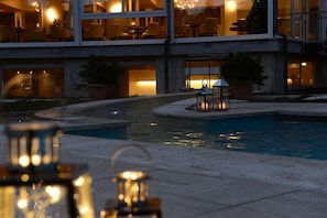 Un hotel con piscina, mobiliario exterior y una entrada bien iluminada.