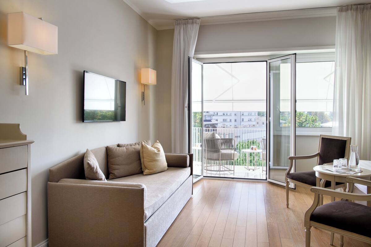 Una habitación de hotel moderna con sofá, una mesa de comedor y un balcón con vistas a la ciudad.