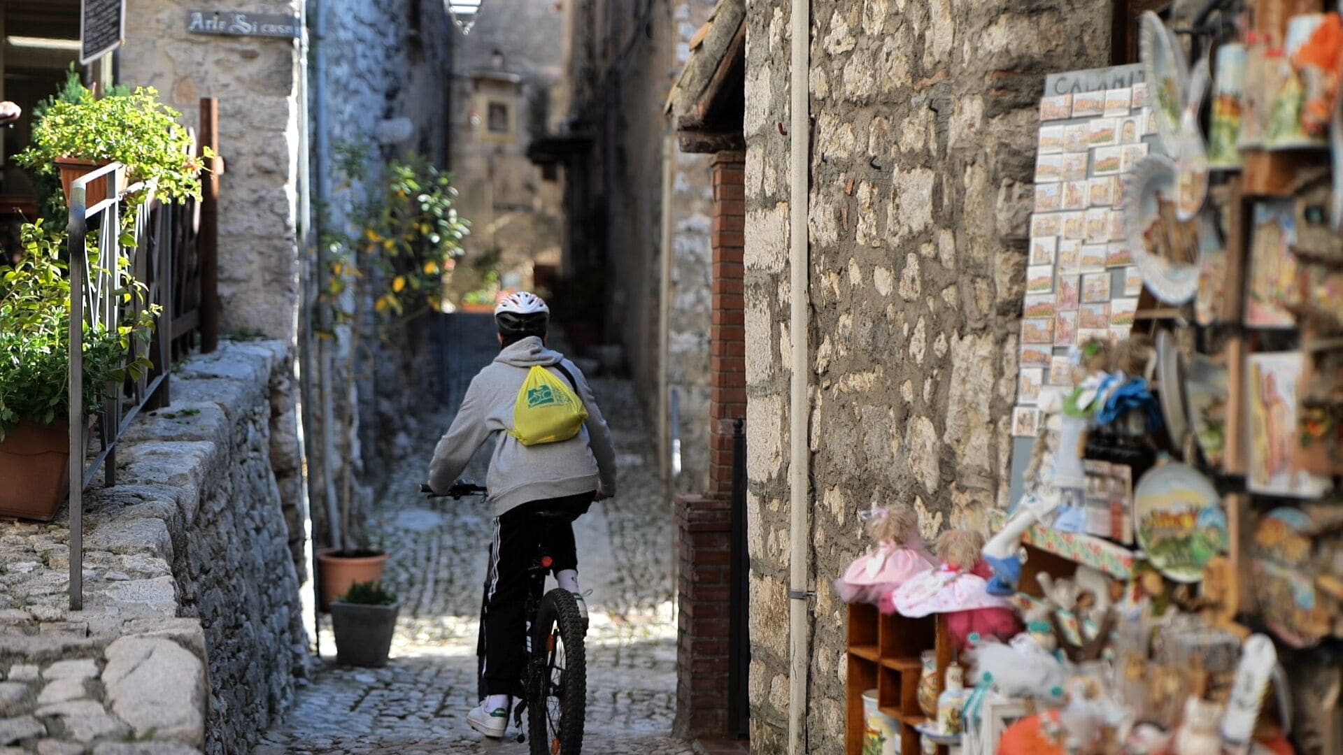 A narrow cobblestone street with a cyclist wearing a helmet and a backpack.