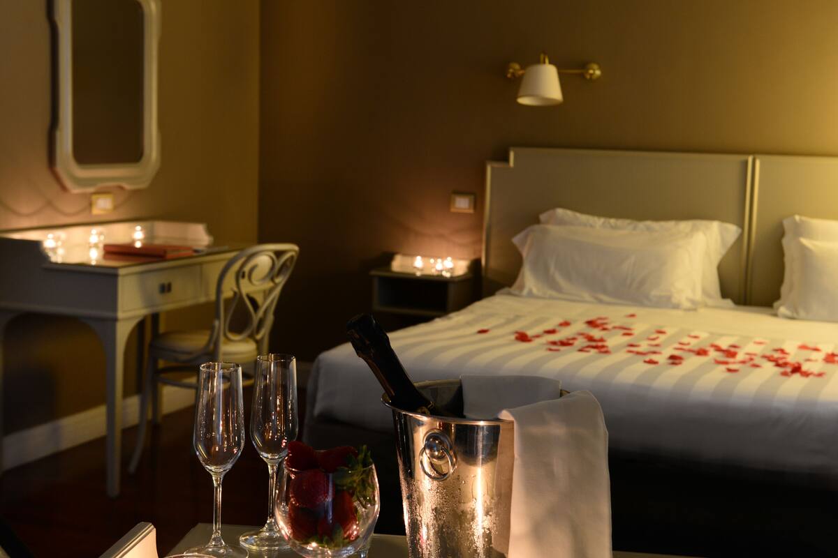 Habitación de hotel con cama, mesita de noche y escritorio con silla. Hay velas sobre la mesita de noche y una botella en el escritorio.