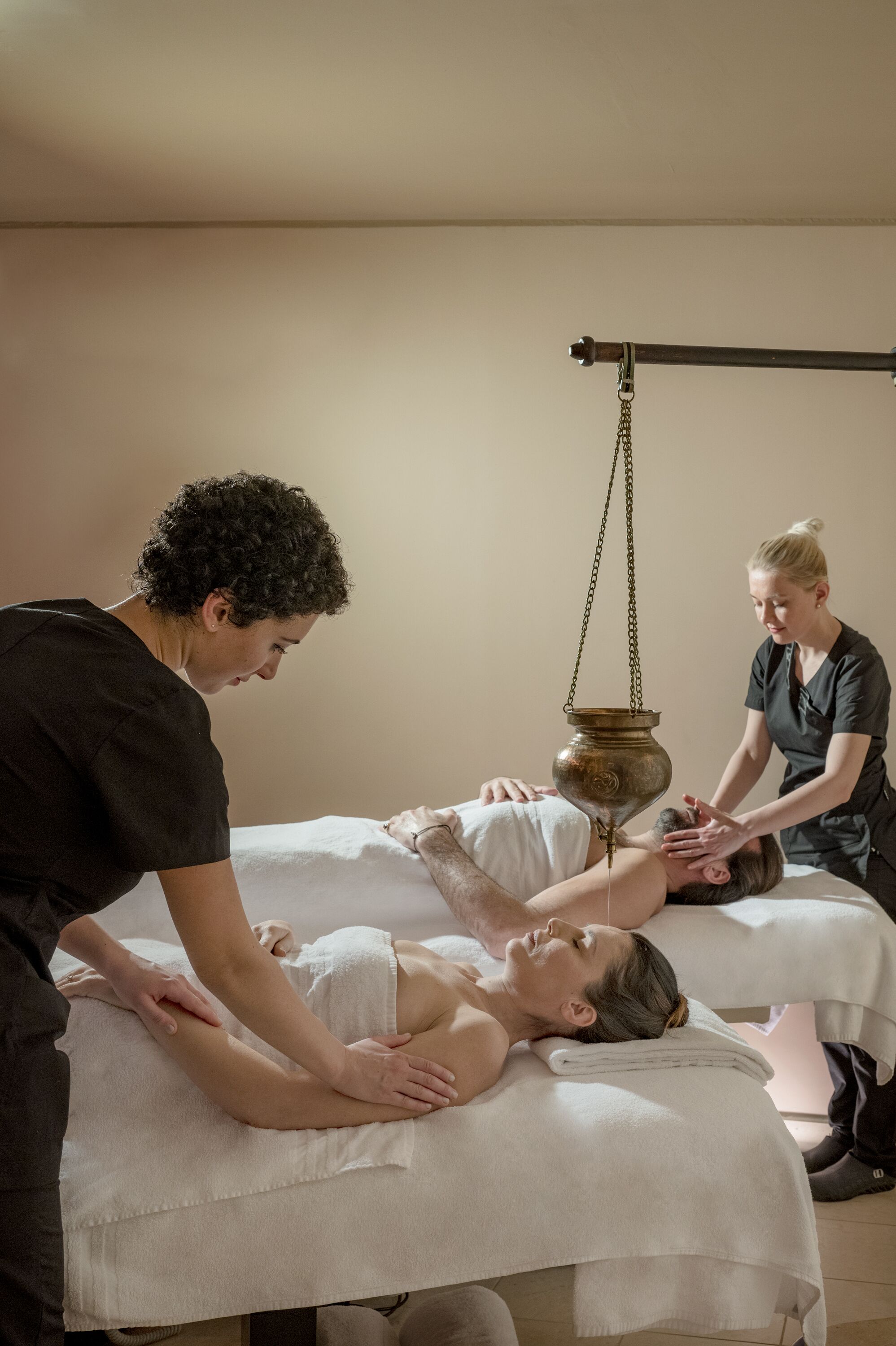 A massage therapy room with a massage table, a hanging metal pot, and a person receiving a massage.